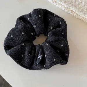 Gros plan détaillé du chouchou en laine noire avec jolis motifs de cœurs et étiquette nœud.