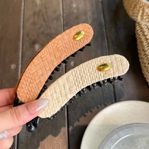 Détail de la pince banane tressée, grand support de queue de cheval au logo doré chic.
