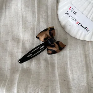 Primer plano de una pinza para el pelo con lazo de leopardo en tela beige con concha.