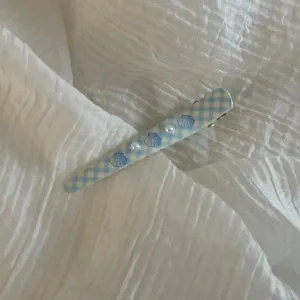 Close-up detail of a cute blue checkered hair clip decorated with tiny pearls and shells.