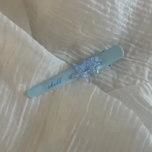 Close-up detail shot of a light blue hair clip featuring cute starfish charms and shell print.