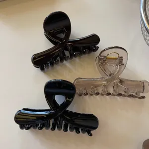 Primo piano di mollette per capelli lucide incrociate, pinze in resina nera e trasparente.