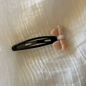 Detalle en primer plano de un bonito pasador de pelo con lazo de acetato rosa sobre tela blanca.