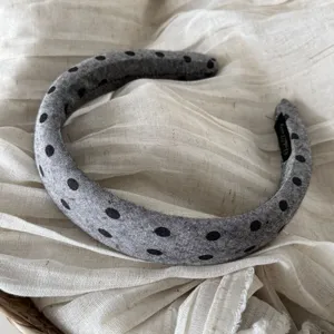 Primo piano di un elegante cerchietto grigio con dettagli classici a pois neri in tessuto.