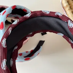 Close-up detail view of pleated fabric wide headbands, textured wine red and blue designs.