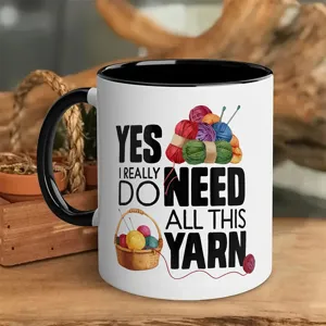 Close-up ceramic coffee mug with funny yarn ball graphic and text design on rustic wooden surface.