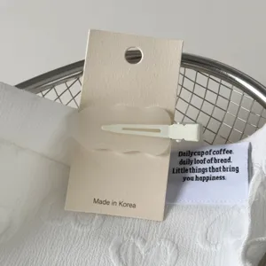 Detailed closeup view of white wavy traceless hair clip with display card and text label