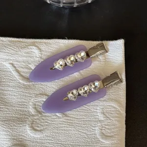 Primo piano di fermagli per capelli viola con strass a cuore e clip metalliche.