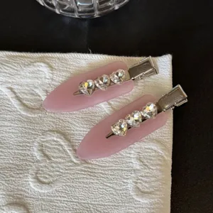 Primo piano dettaglio mollette per capelli rosa in acetato con strass a cuore e fermagli.
