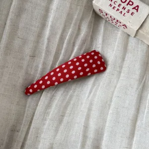 Detailed view of a charming red fabric hair clip with cute white polka dots. Soft and stylish.