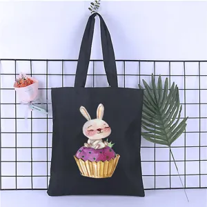 Detail view of black canvas tote bag featuring cute watercolor rabbit and cupcake print scene.