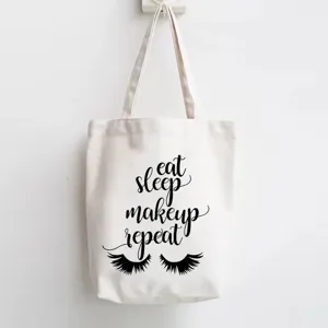 White canvas tote bag with chic makeup quote print and eyelash graphic, casual shoulder bag.