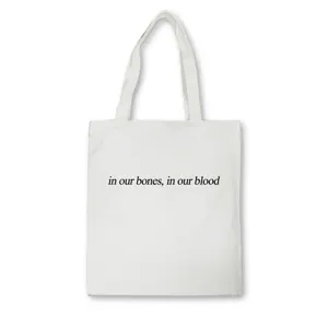 Detail shot of white canvas tote bag featuring black typography print. Simple aesthetic.