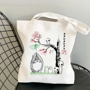 Detail shot of white canvas tote bag with Ghibli anime ink print, casual shoulder handbag.