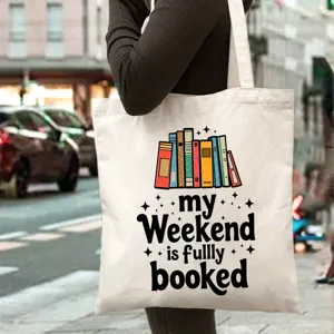 Vista detallada del bolso tote de lona blanca con estampado de libros y texto al hombro.