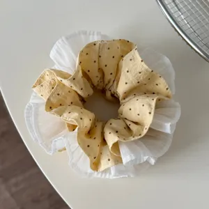 Detailed shot of yellow polka dot hair scrunchie with white ruffled lace edge, soft fabric.