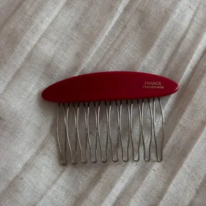 Detail view of red acetate hair comb with metal tines, featuring fine craftsmanship and polished finish.