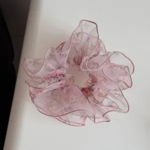 Close-up detail van de roze bloemige, transparante stoffen haarelastiek met geruffleerde randen.