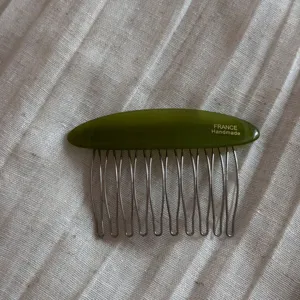 Close-up detail of green acetate side comb, featuring metal tines and glossy finish.