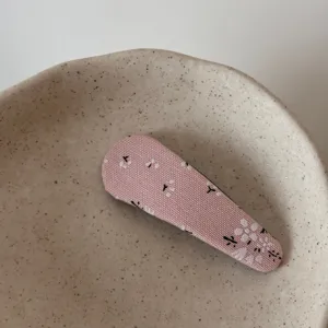 Close-up detail shot of a cute pink floral fabric hair clip placed inside a speckled ceramic bowl.