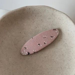 Close-up detail shot of a cute pink floral fabric hair clip resting on a stylish speckled dish.