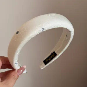 White padded headband for women featuring delicate daisy embroidery, elegant hair accessory.
