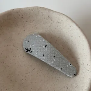 Close-up detail of grey fabric snap hair clip featuring cute floral print and delicate embroidery.