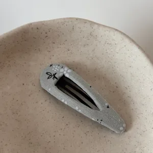 Detailed shot of fabric-wrapped BB hair clip with floral embroidery on ceramic dish.