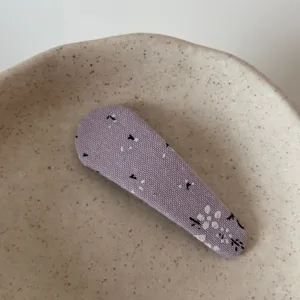 Close-up detail of a cute purple floral fabric snap hair clip resting on a ceramic dish.