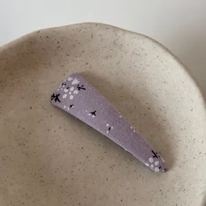 Close-up detail of a purple floral fabric hair clip placed on a minimalist ceramic dish.