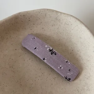 Detailed shot of a stylish purple fabric hairpin with delicate embroidered floral patterns.
