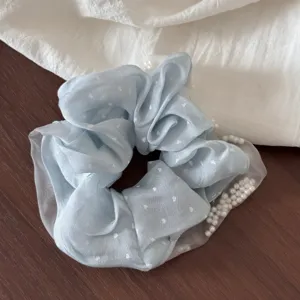 Detailed close-up of a light blue fabric hair scrunchie with white heart pattern and elegant pearls.