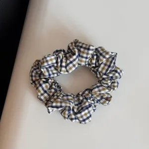 Primo piano dettagliato di un elegante elastico per capelli in tessuto a quadri blu, bianco e giallo.