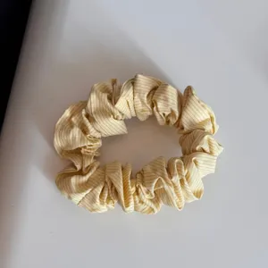 Vista dettagliata di un elastico per capelli in tessuto a righe gialle con trama plissettata.