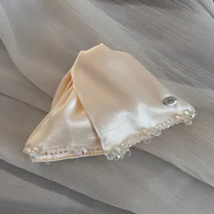 Detailed shot of a champagne satin hair clip with delicate beaded edge and metal handmade tag.