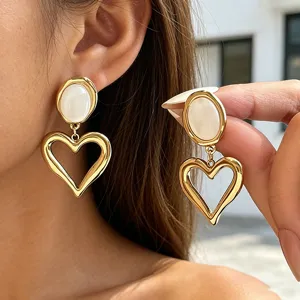 Close-up detail of gold-toned hollow heart earrings featuring a chic white opal stone stud.