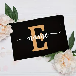 Custom black canvas makeup bag with gold letter E and white name print, floral backdrop.