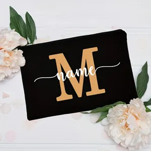 Close-up detail of custom black canvas pouch featuring gold letter M and white name print.