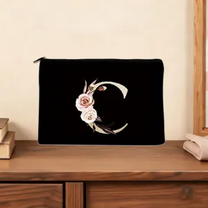 Detail view of a black cosmetic pouch featuring a floral letter C print on a wooden desk.