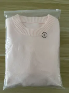 Pink knitted sweater detailed shot, folded neatly in clear bag, cozy autumn wear.