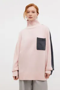 Detailed view of the cozy pink loose turtleneck knit sweater featuring dark grey pockets.