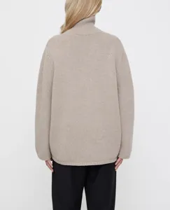 Detailed view of women's loose turtleneck wool sweater in oatmeal color, cozy autumn knitwear back.
