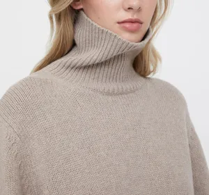Detail shot of a cozy beige turtleneck sweater featuring soft ribbed knit texture and comfortable fit.