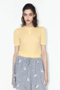 Close-up detail of yellow short sleeve polo knit sweater featuring delicate texture.