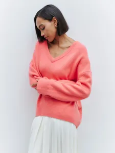 Close-up detail of a soft pink V-neck knit sweater worn by a model with white pleated skirt.