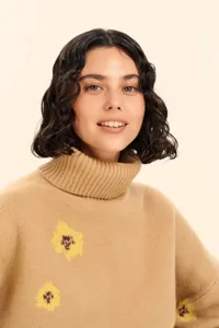 Detailed close-up view of camel turtleneck sweater featuring yellow floral jacquard knit design.