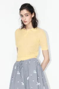 Detailed view of women short sleeve yellow polo knit sweater paired with a floral skirt.
