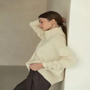 Side profile detail of a woman wearing a cozy beige high-neck knit sweater leaning against wall.