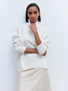 Close-up detail of women's white turtleneck knit sweater and skirt in clean studio setting.