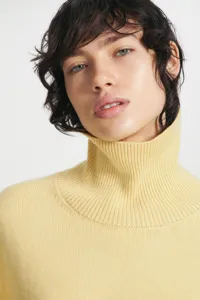 Close-up detail of a stylish women pale yellow turtleneck knitted sweater, soft ribbed collar design.